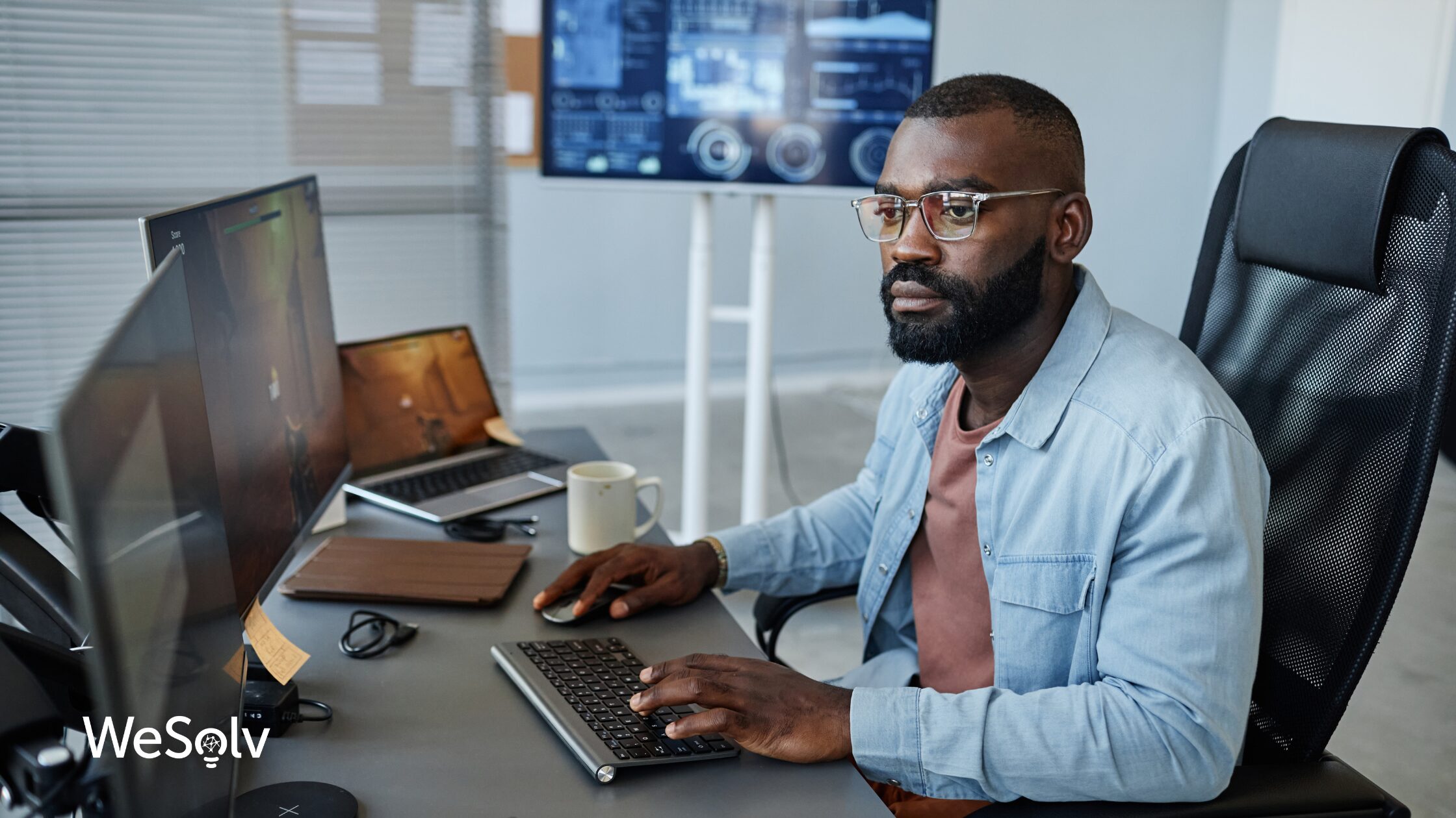 Black man in a denim shirt working at his computer.